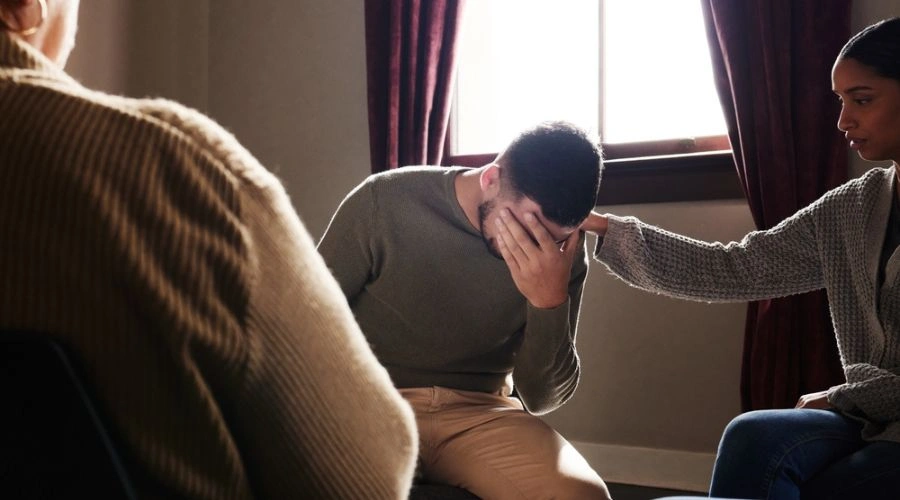 Image of a male in group therapy with hand on his face being consoled by a female next to him - Supporting Mental Health During Recovery