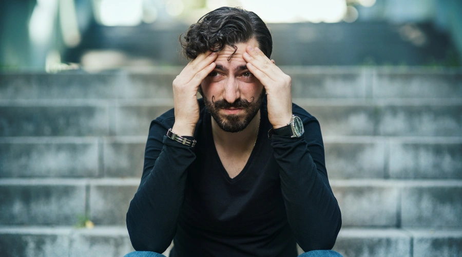Image of a man sitting and holding his hands on his head,  experiencing kratom withdrawal symptoms, including restlessness and fatigue